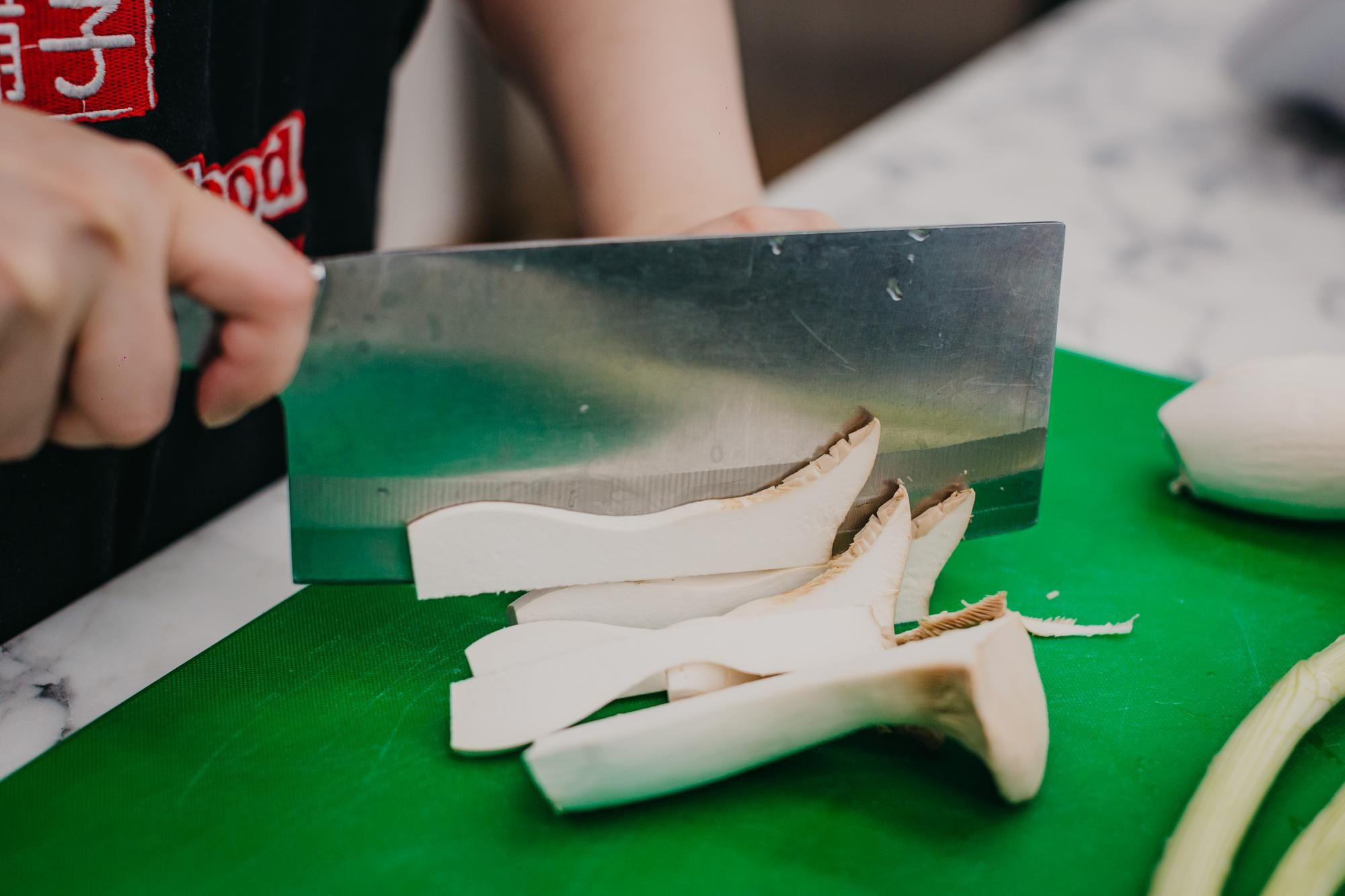 Close up of a person chopping a large mushroom with a Chinese cleaver