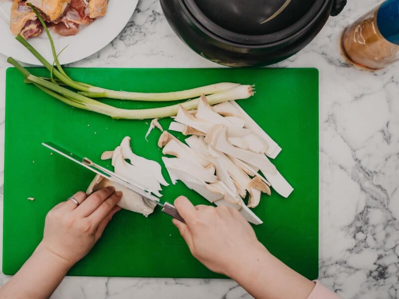 Overhead shot of a person slicing large mushrooms on a green cutting board