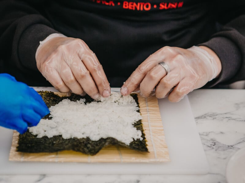 Two pairs of hands work on filling and hand rolling sushi.