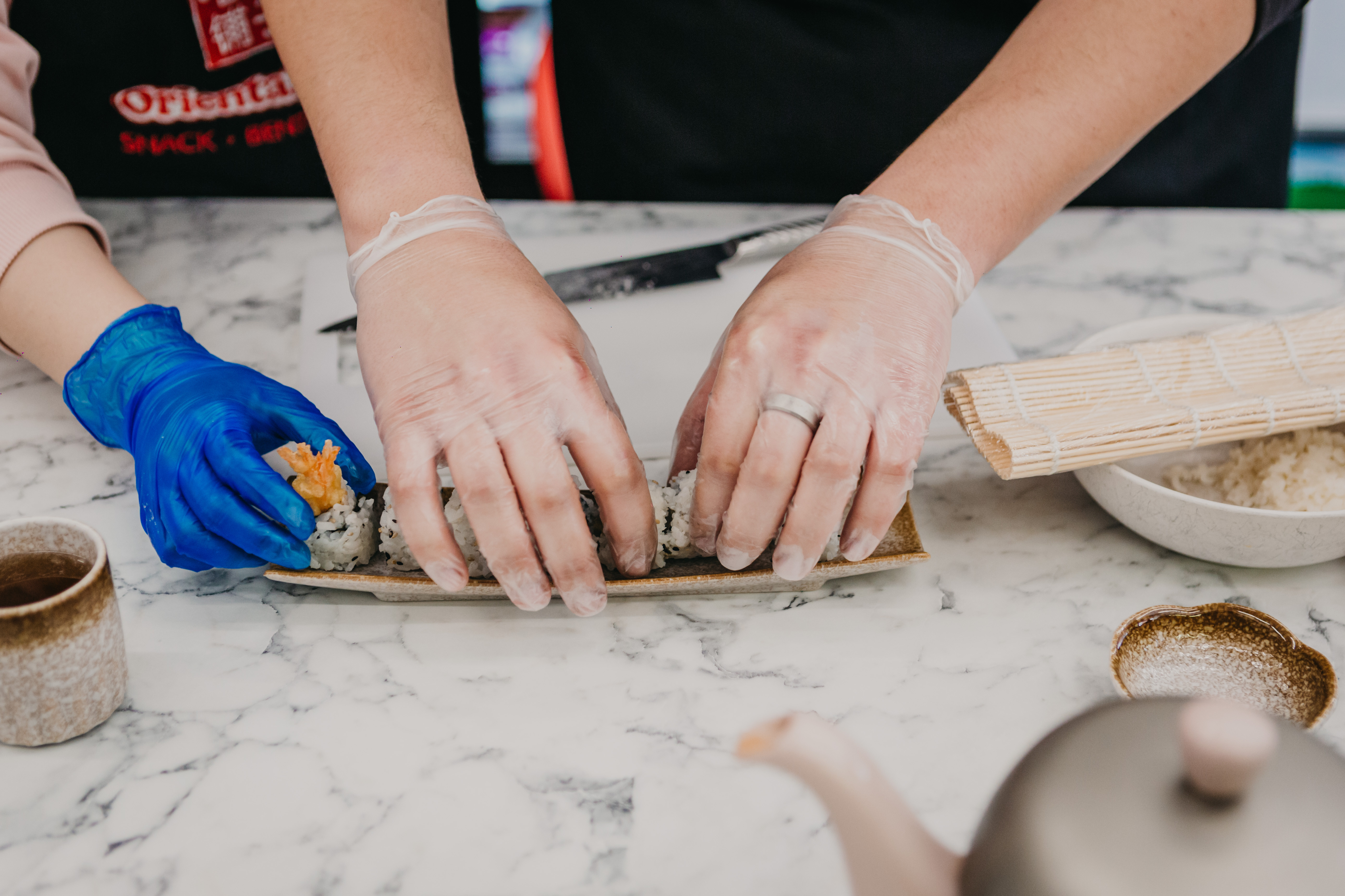 Close up of someone helping a cooking student roll sushi