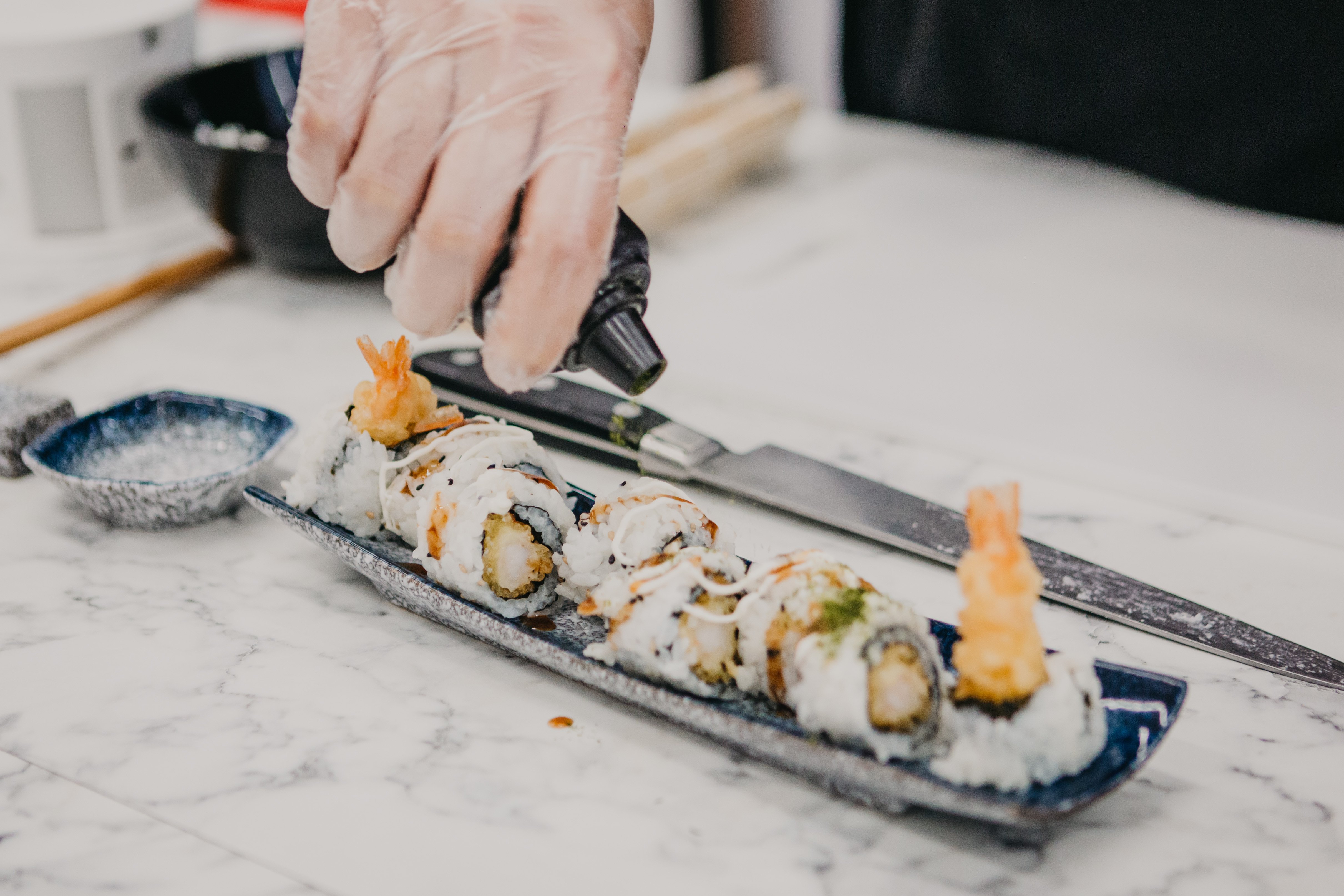 Close up of a person adding garnish to a plate of sushi rolls