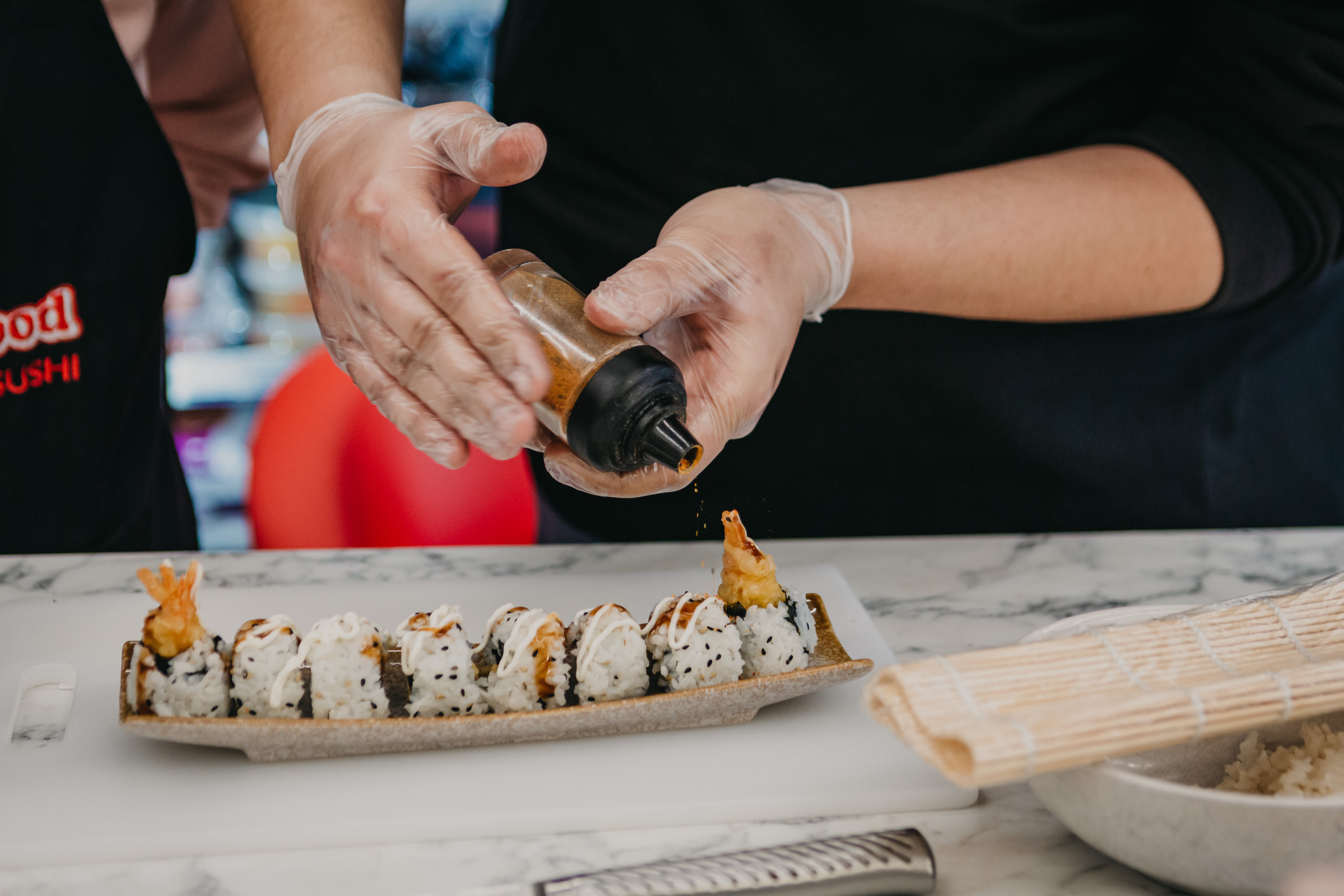 Person applying seasoning to a row of sushi rolls