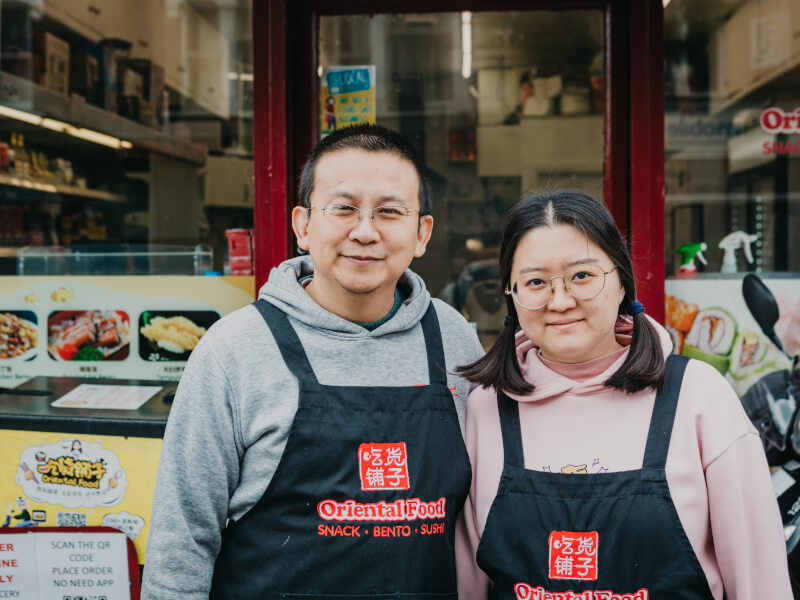 A man and woman are standing outside an Oriental food store