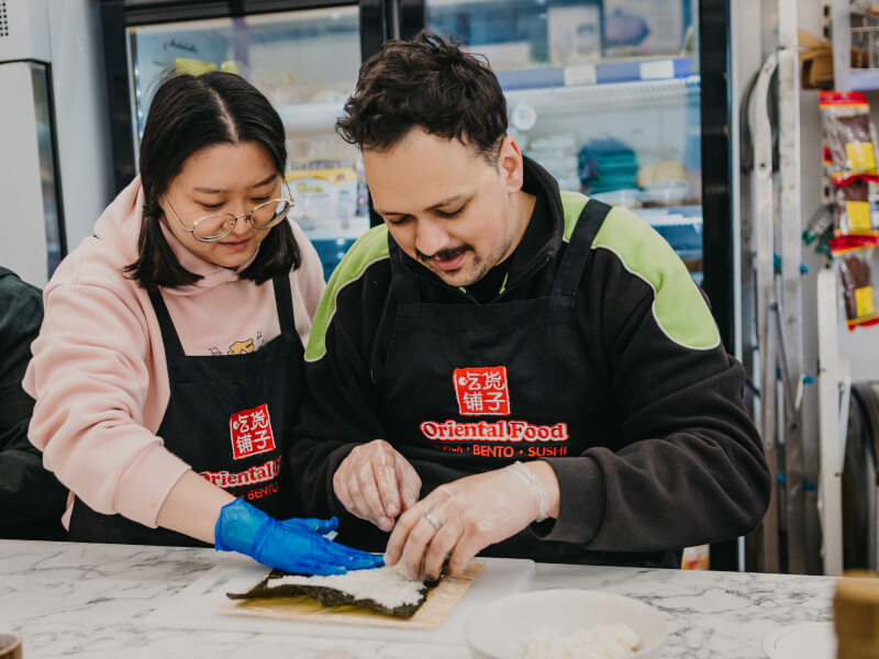 A man and woman rolling sushi in a sushi class