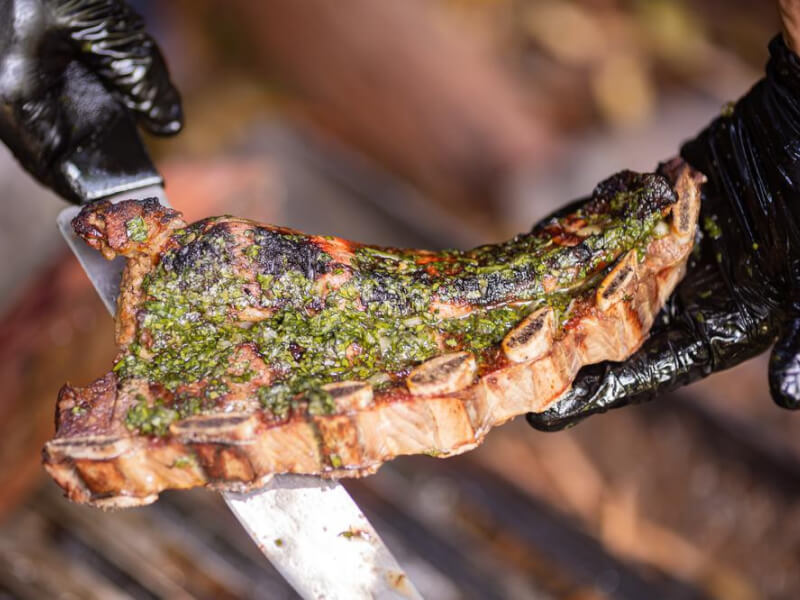 A rack of ribs cooked with a rub of green herbs and spices, being held over a grill rack