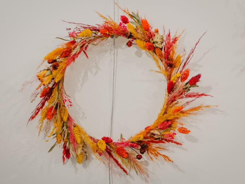 A red and orange DIY Christmas wreath on a white wall.