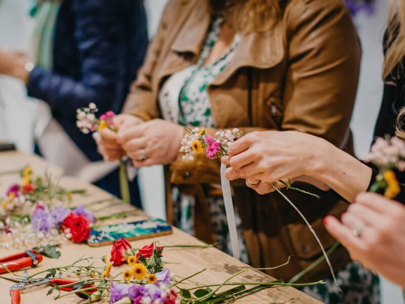 A close up of several hands experimenting with flowers in a floristry course.