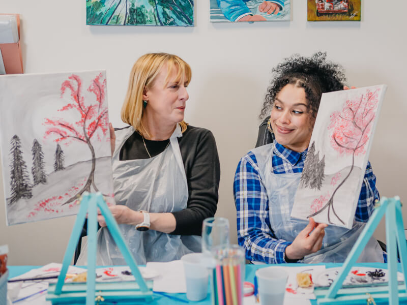 A mother and daughter show off their paintings from an paint and sip class.