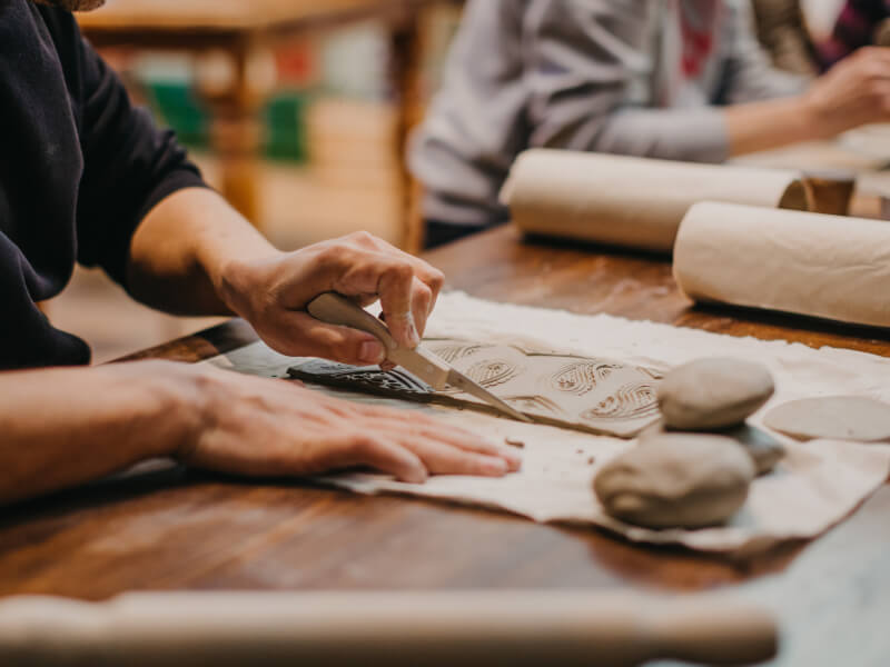 A person using pottery tools on clay at a pottery class.