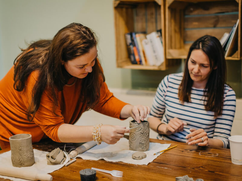 A woman helps another woman at a clay sculpting class