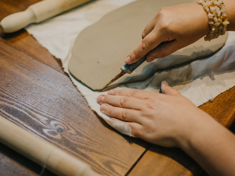 A person creates slabs out of clay in their pottery making class.