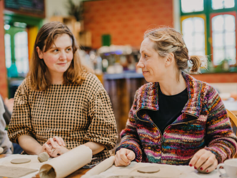 Two women smiling at each other at a pottery class.