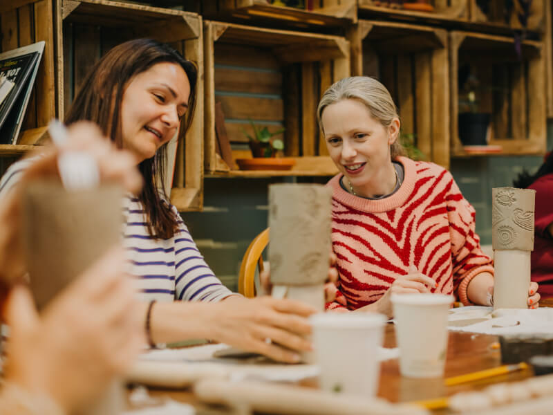 Woman looking at another woman's clay sculpture at a pottery class.