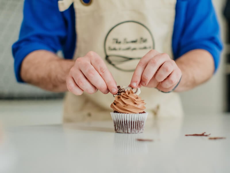 A person is adding edible decorations to a handmade cupcake