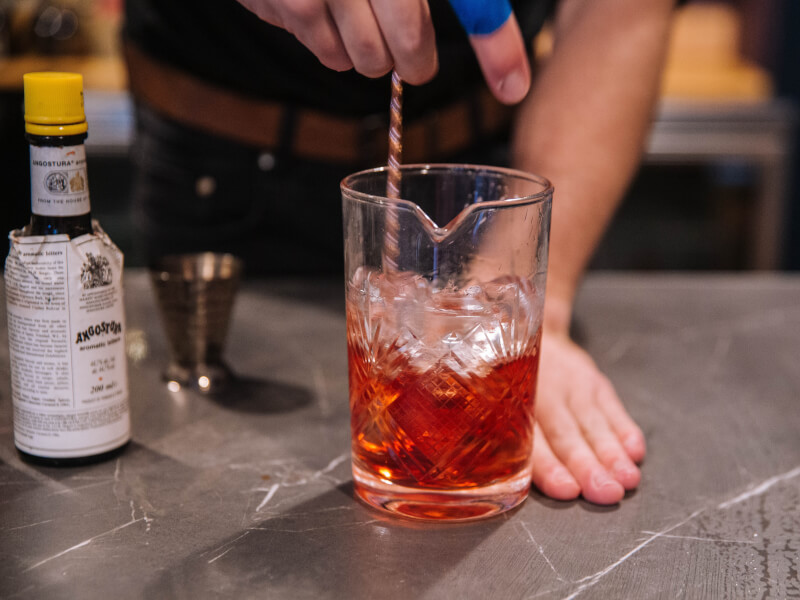 A person stirs an orange liquid with ice in a jug
