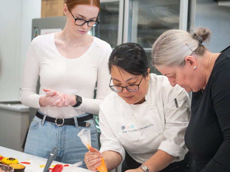Two women learning from their teacher at a cake making class