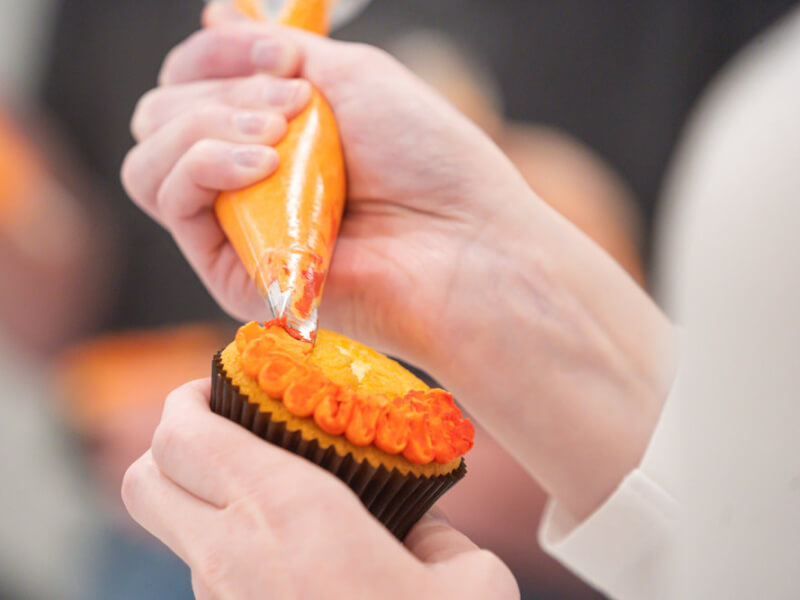 Close-up of hands piping orange icing in a cupcake decorating class.