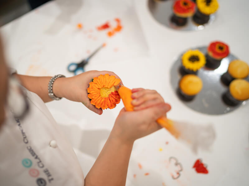 Someone adding orange buttercream to a cupcake at a cake decorating class.