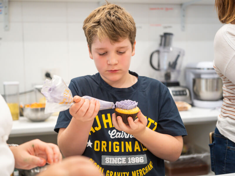 Child concentrating whilst using piping bag to decorate cupcake.