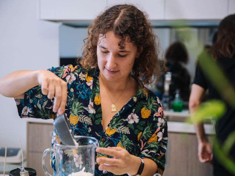 A woman in a floral top pouring candle ingredients into a container