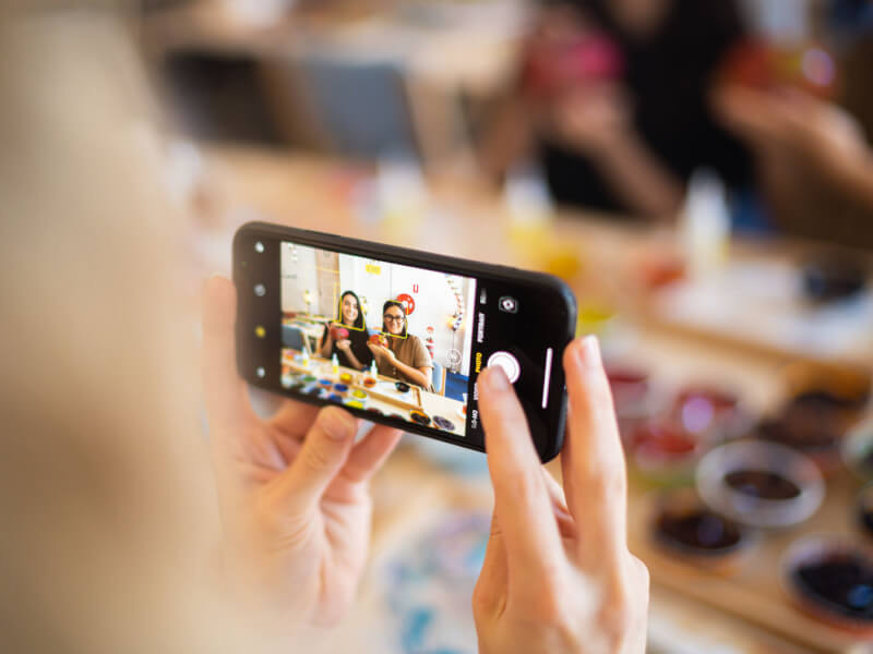 A person is taking a photo of two women at a craft class on a smartphone