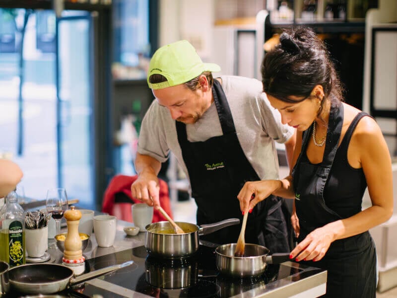 Two people wearing black aprons stiring saucepan at cooking class