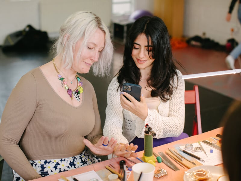Two women smiling taking photo of their handmade rings