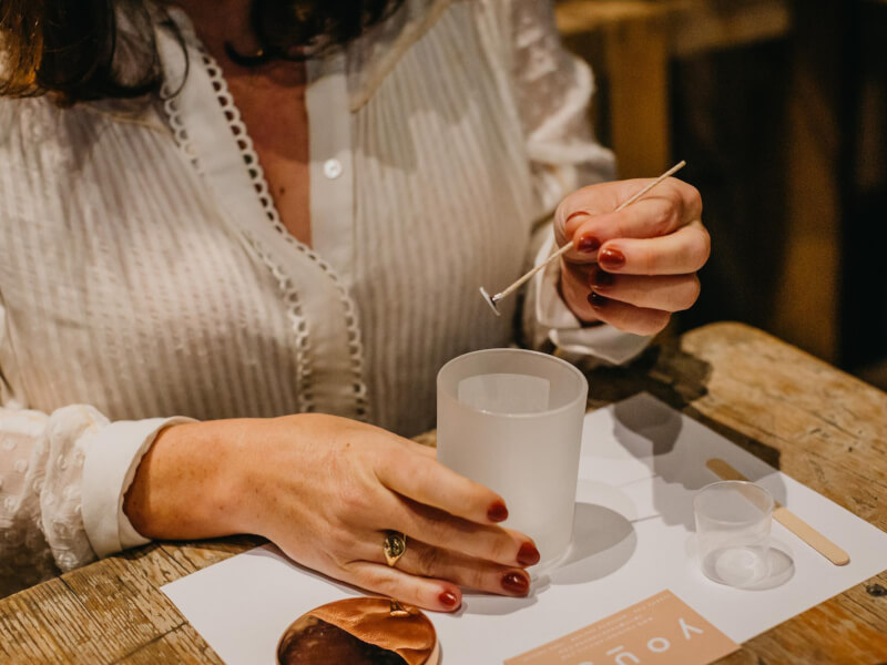 A close up of a woman assembling a homemade candle in a glass jar