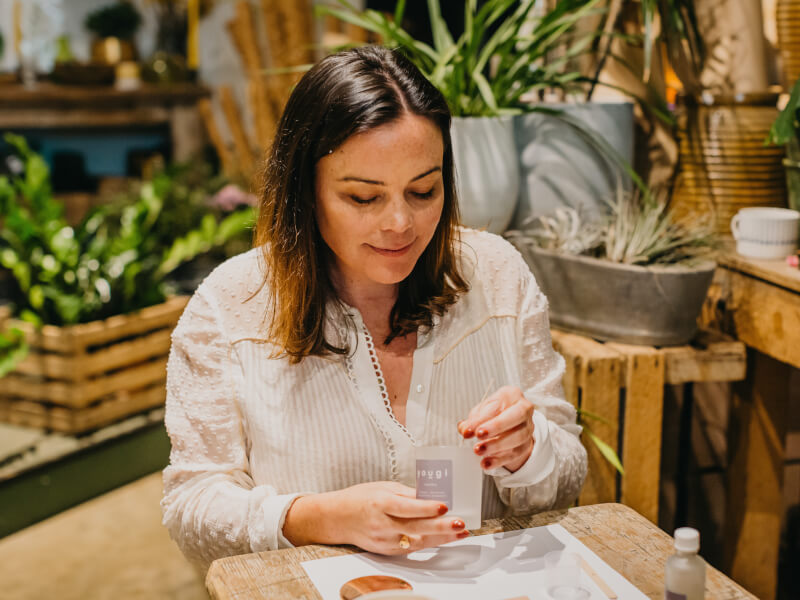 A woman looking down to insert a candle wick into a glass candle holder with a label on it