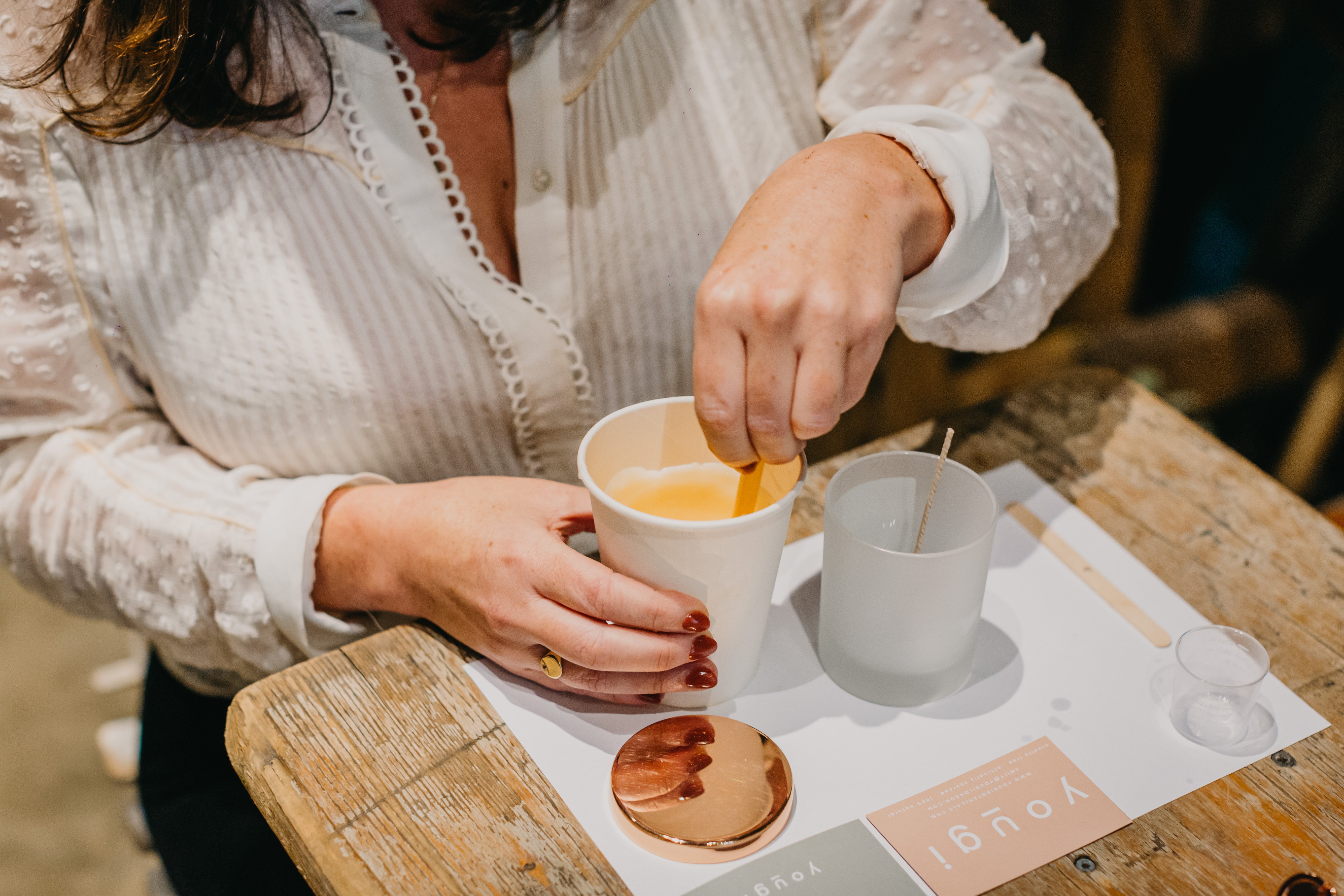 Close up of a woman in a white blouse making a container candle
