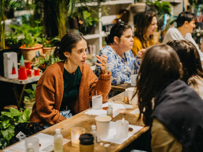 A group of women sitting around a table talking while making candles