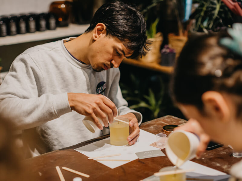 A man makes a DIY candle by pouring scented wax into a container.