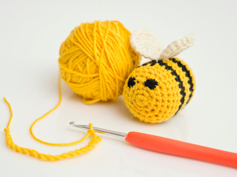 A crocheted amigurumi bee with yellow yarn and an orange-handled hook
