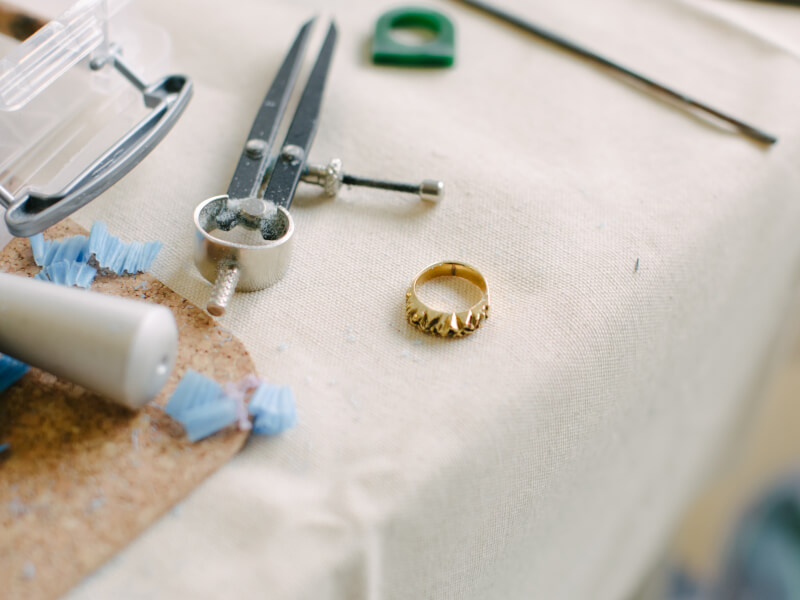 A finished handmade gold ring sitting on a white tablecloth