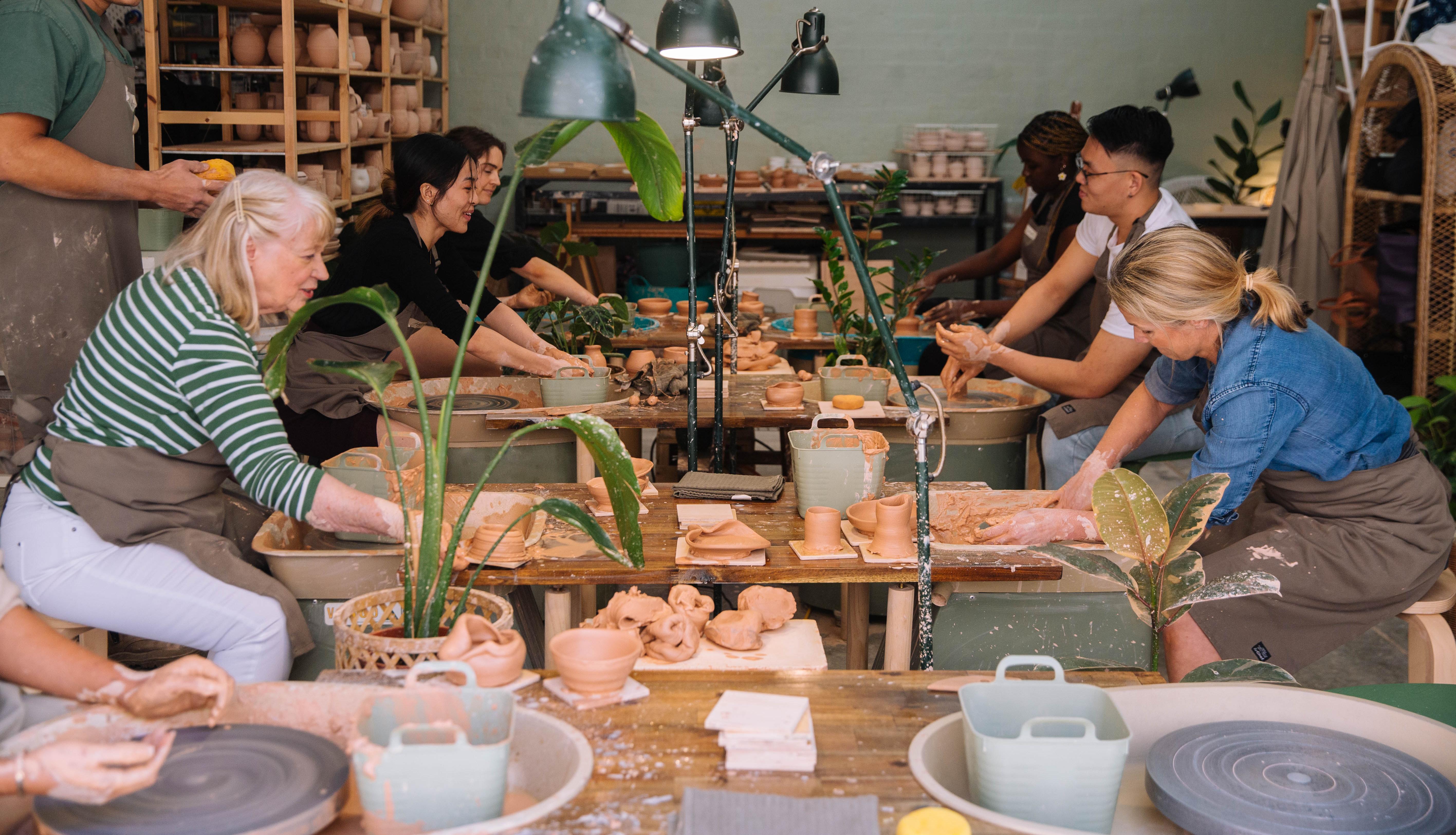 A group of people are trying wheel throwing at a pottery class