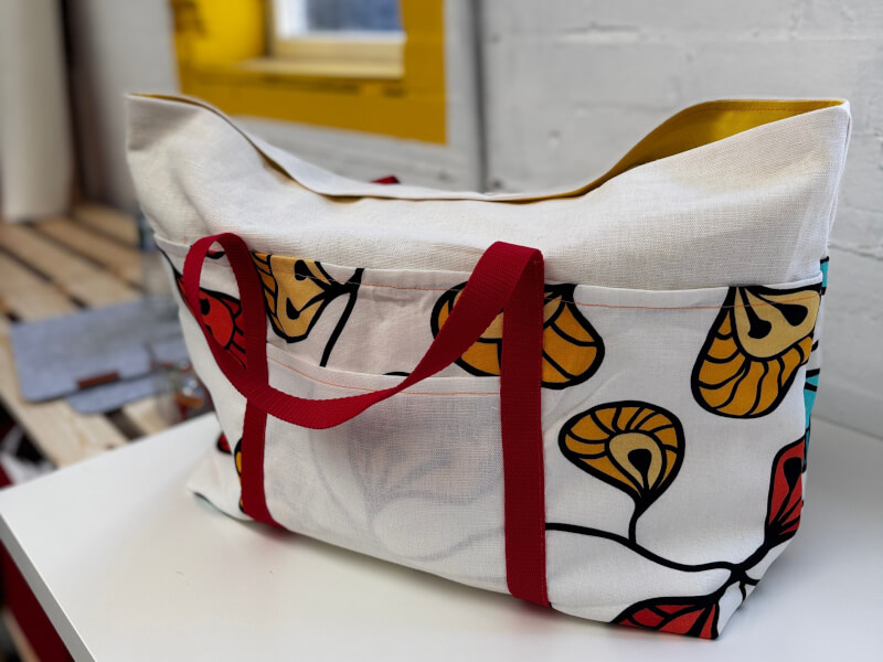 A white handmade canvas bag with red strap sits on a table