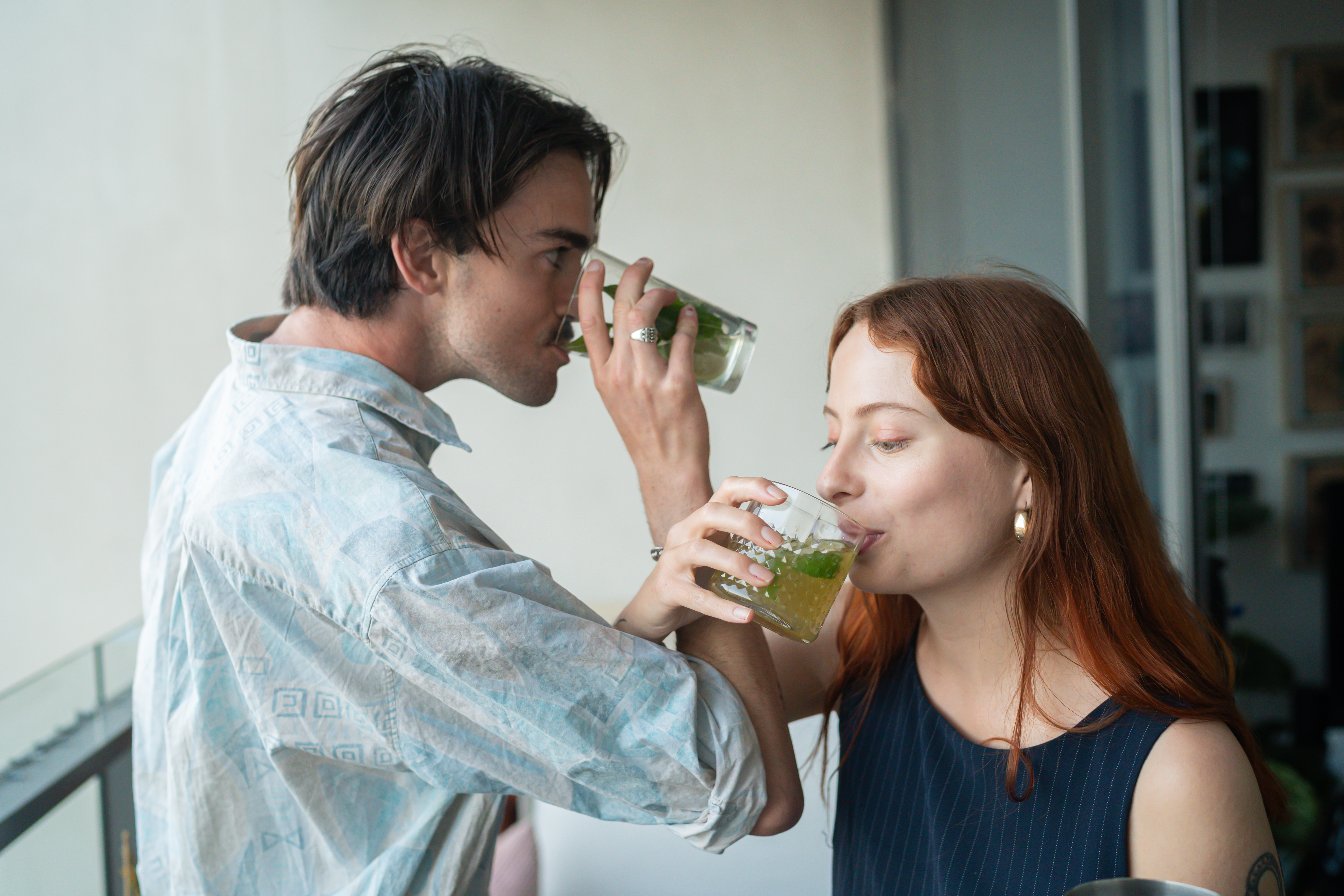 A man and woman are drinking cocktails with their arms entwined