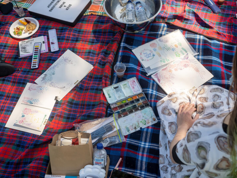 A selection of art supplies and snacks on a tartan blanket