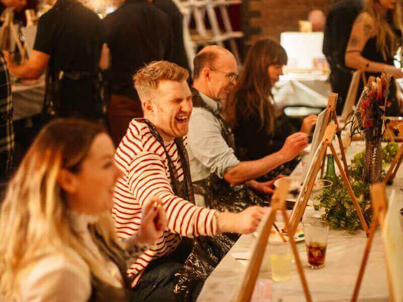 Man laughing with friends in a painting class