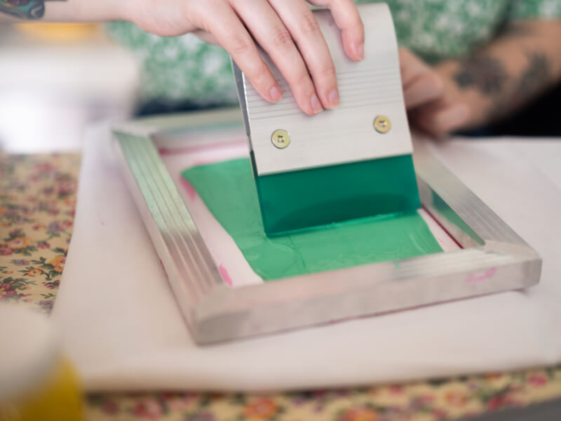 A close up of a person making a screenprint with green ink
