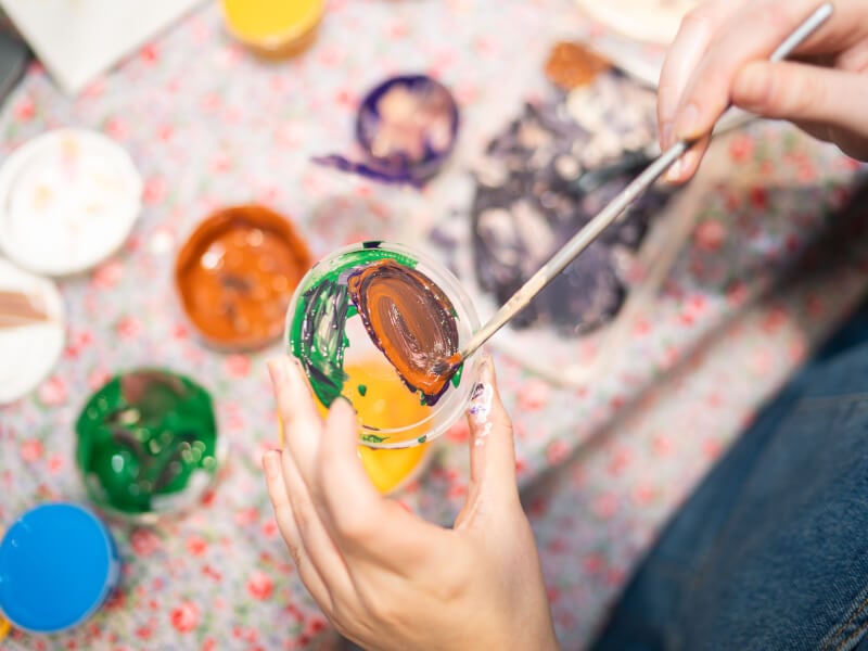 A person mixing paints on a small tray using a paintbrush