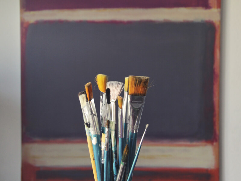 Several paintbrushes with a painted canvas in the background