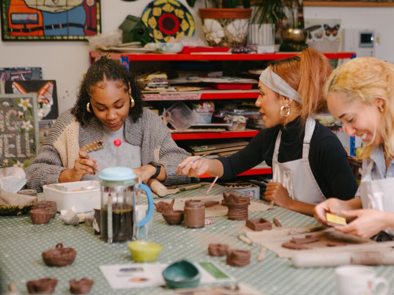 A group of women sit at a table at a terracotta pottery workshop, making pots