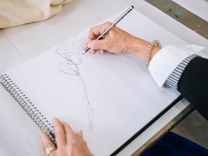A close up of a person drawing flowers in a sketchbook