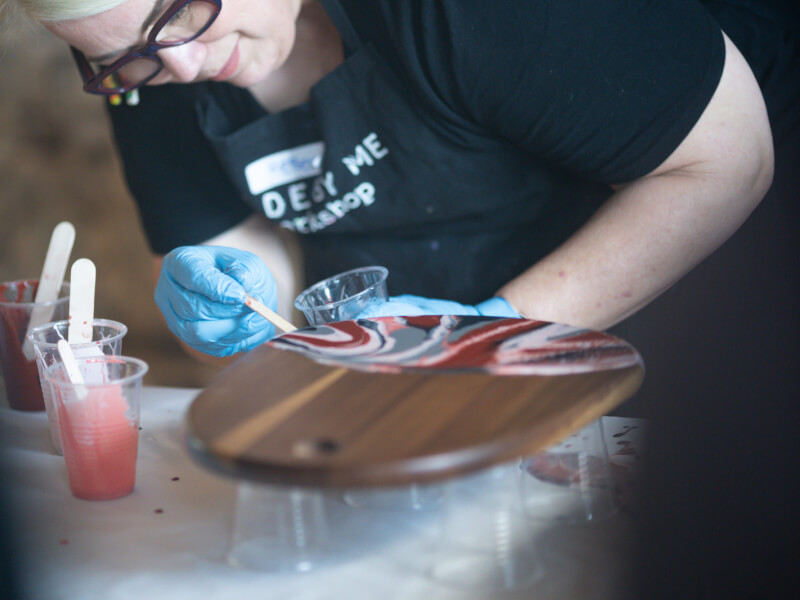 A person is decorating a wooden chopping board with the paint pouring technique
