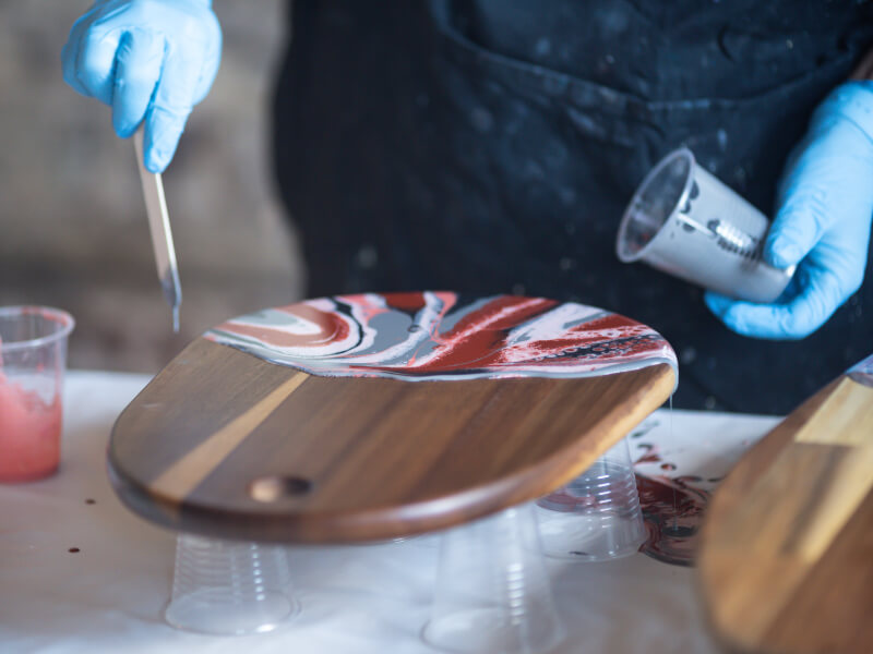A person is decorating a chopping board using the paint pouring technique