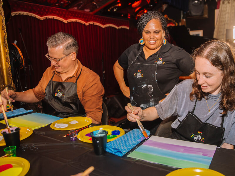 A man and woman are painting coloured stripes across canvas