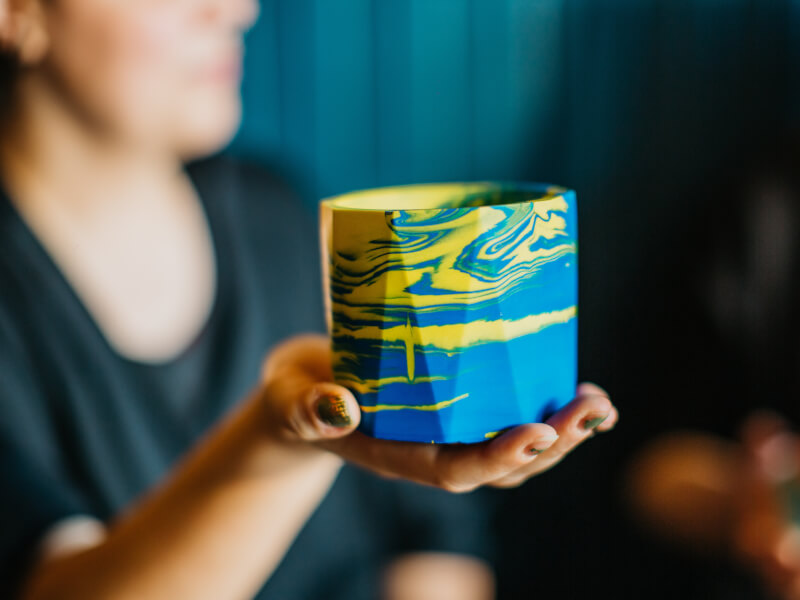A person is holding a blue and yellow resin art plant pot in the palm of their hand