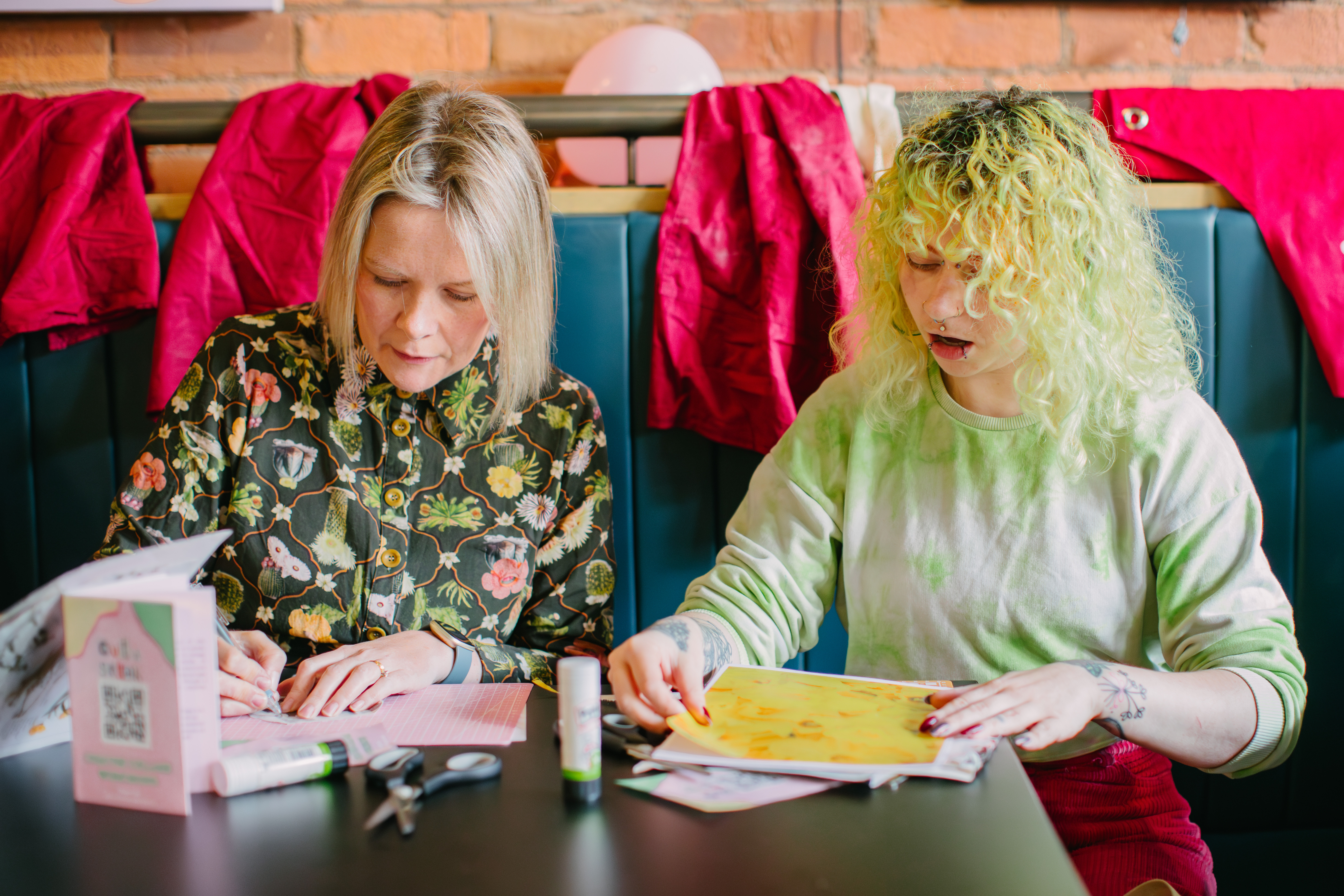 Two women are sitting at a table, creating collages with paper 