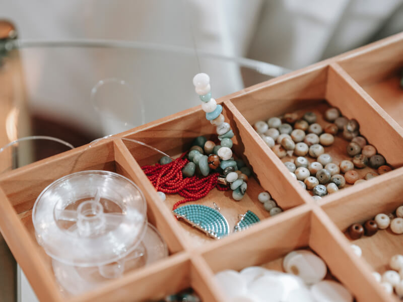 A wooden box filled with beads, embellishments and string sits on a table